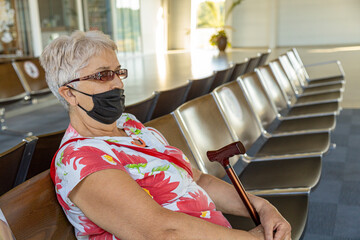 Senior woman sitting in the airport waiting area wearing handmade face mask. Travel restrictions...