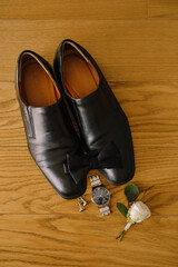 Black mens shoes and bow tie on wood texture with cufflinks, wristwatch and white rose groom boutonniere.