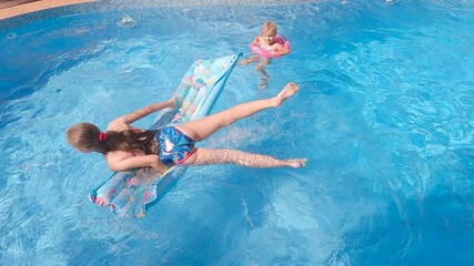 Sisters swims in the pool on a swimming circle and water mattress