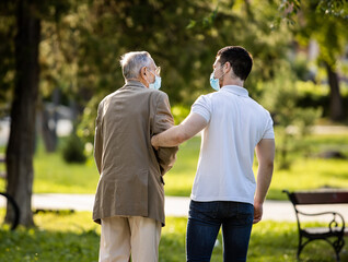 Grandfather and grandson spending quality time in park talking and walking with covid masks