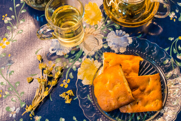 Cup of fresh flower and herb arabic tea and some Tasty and healthy almond cookies, rich in vitamins and less sugar. copy space.Top view on a blue flowers background..