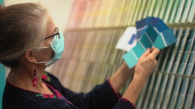 Woman wearing face mask looking at paint chips in a hardware store. Concept of cornonavirus shopping experience.