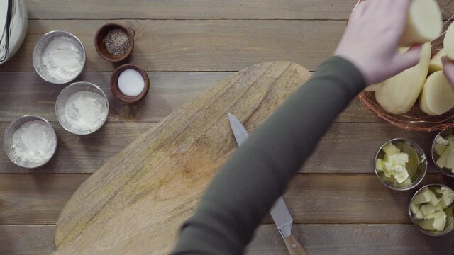 Time lapse. Flat lay. Slicing organic gold potatoes on a V-blade mandoline to prepare scalloped potatoes.
