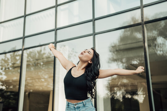 Portrait of excited happy young sensual woman screaming. Lady raises arms from joy, shouts loudly, dressed in singlet and jeans. Image with copy space. Celebration concept.