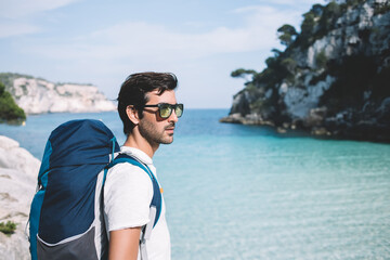 South Asian wanderer in touristic clothing standing at rocky near oceania bay enjoying breathtaking...