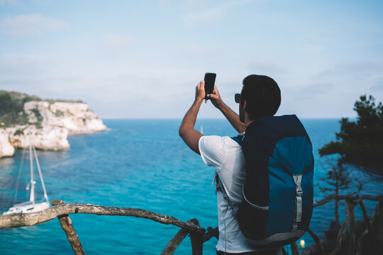 Faceless man taking picture of majestic seascape