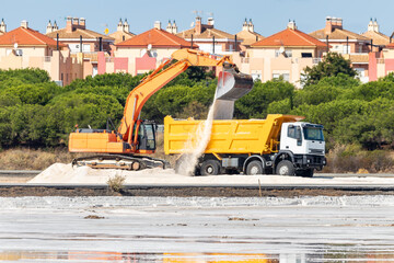 Excavator loads salt into a truck. Traditional Sea salt production is salt that is produced by the evaporation of seawater.