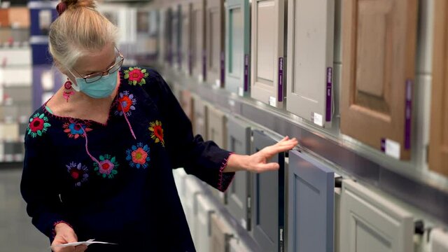 Closeup of blond woman wearing face mask looking at kitchen cupboards in a big box hardware store.