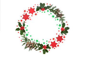 Festive Christmas holly & cedar abstract wreath with red & green star decorations on white background. Holiday symbol for the xmas season. Top view, flat lay, copy space.