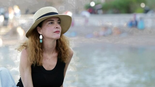 Portrait of a woman 40-45 years looking away wearing casual clothes and a straw hat against sea, pensive, thinking.