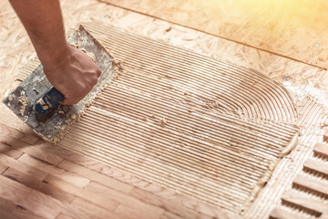 Laying hardwood parquet. Worker installing wooden laminate flooring. Putting glue on the floor....