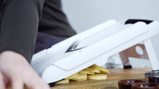 Slicing organic gold potatoes on a V-blade mandoline to prepare scalloped potatoes.