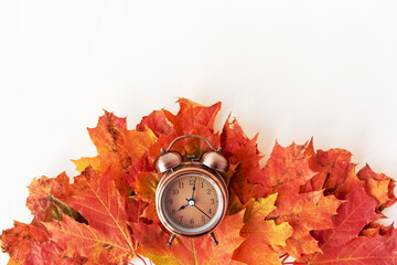 Elegant vintage alarm clock in metal case lying on pile of red and yellow dry autumn leaves with template for design on white color background upper view.