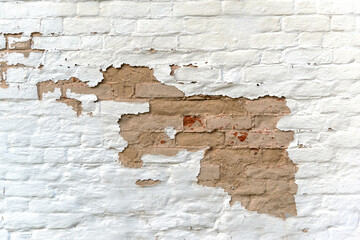 Textured surface of abandoned building wall made of weathered brown bricks covered with flaked white color stucco at bright sunlight extreme close view