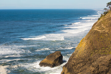 The Pacific Ocean coastal rocky beach shoreline with blue sky horizon and crested white foamy ocean waves.