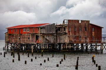 Vintage old and worn abandoned cannery building on Columbia River with moody cloud sky and rippling water.