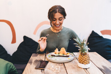 Fototapeta na wymiar Cheerful young woman enjoying bruschetta with salmon while sitting in cozy restaurant