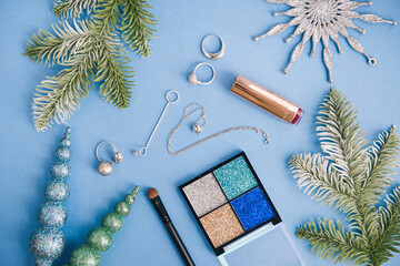 flat lay composition on color background. New year celebration accessories - glitter shadows, silver rings, brush and christmas decor.