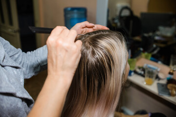 Fototapeta premium Master hairdresser combs the hair of a young woman, blonde. Haircut. Home beauty salon. 