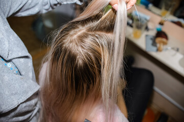 Fototapeta premium Master hairdresser combs the hair of a young woman, blonde. Haircut. Home beauty salon. 