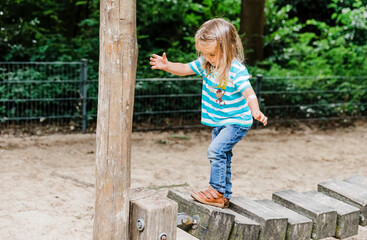 Toddler girl walking on wooden playground equipment
