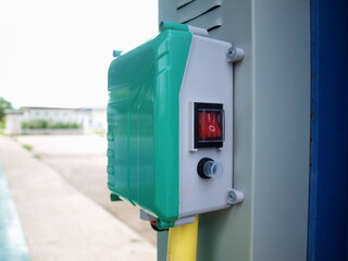 Switch box beside the control cabinet. The green plastic box has a red on-off switch with a power cut button. On a cement patio background on a sunny day with a copy space. Selective focus