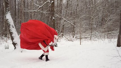 Santa claus with big Christmas or New Year sack of gifts in winter forest.