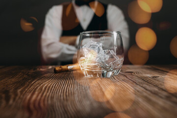 Bartender in a dark leather apron puts three glasses of whiskey on a dark wooden bar in a nightclub. Close-up. Spa ce