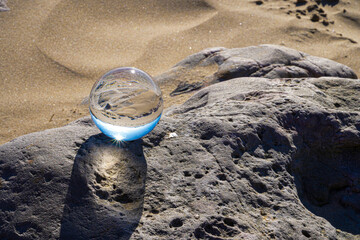 Fototapeta na wymiar Photography Crystal Photo Ball showing upside down reflection of sky beach and waves balanced on rocks on sandy beach.