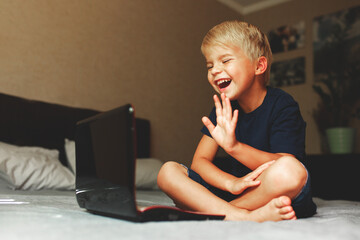 child does homework , lying in bed using his laptop or skyping.