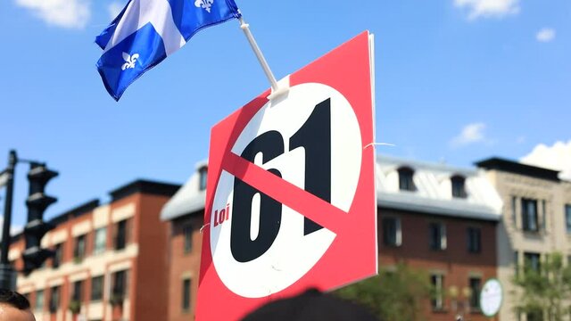 Selective focus of man hand holding poster with quebec flag wanting to boycott law 61 during protest march on downtown street