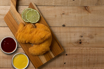 breaded chicken filet, served with mustard and ketchup, on a wooden background. top wiew
