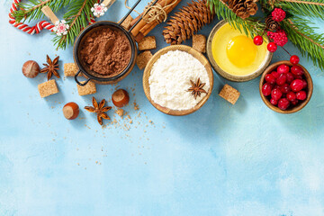 Seasonal baking winter. Ingredients for Christmas baking - cocoa, cranberries, spices, nuts, flour and eggs on a blue stone background. Flat lay. View from above. Copy space.