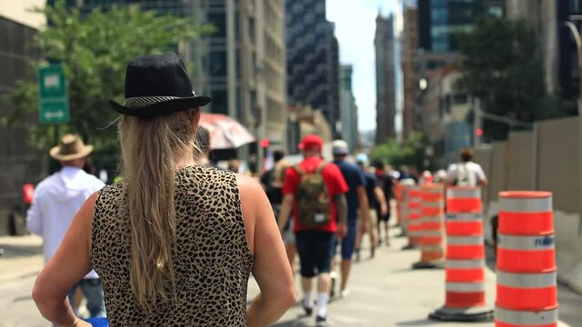 Rear view of young female wearing hat and raised hand walking with pram on street with crowd during protest against public health guidelines