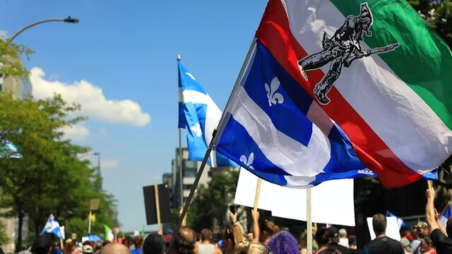 Selective focus of people holding patriot flag, and quebec country flag waving high in the air during protest march against fake news in downtown city