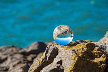 Fototapeta na wymiar Photography Crystal Photo Ball showing upside down reflection of sky beach and waves balanced on rocks on sandy beach.