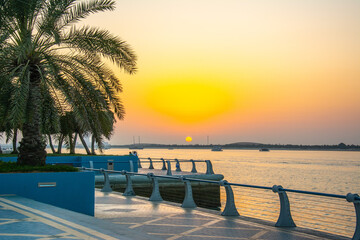 The view of the Persian Gulf, Corniche promenade with palm trees on sunset in Abu Dhabi, United Arab Emirates