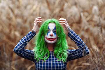 Portrait of a greenhaired girl with joker makeup on a orange leaves background.