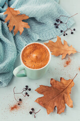 Blue cup of coffee with autumnal dry leaves and dry berries on a light background. Autumn mood concept.