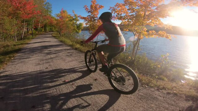 Biking in Fall. Mountain biker riding MTB bicycle on forest gravel in Autumn foliage with colorful leaves. Woman living healthy lifestyle. Petit train du nord, Mont Tremblant, Quebec, Canada