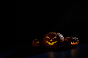 Halloween card. jack o lantern with candles glow on a black background. A row of creepy pumpkins with carved grimaces smokes in the dark.