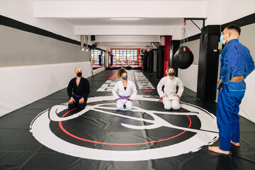 Martial arts students with kimonos on the gym floor mat listening to their teacher's instructions...
