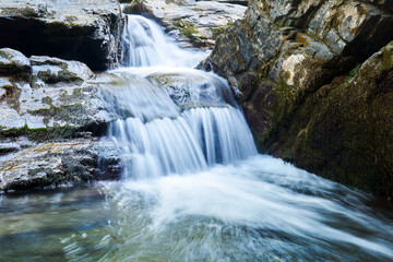 Fototapeta premium small waterfall in a mountain stream between rocks, the water is blurred in motion