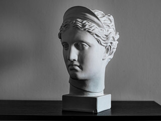 Gypsum copy of ancient statue Diana head on a dark textured back. Plaster sculpture woman face.