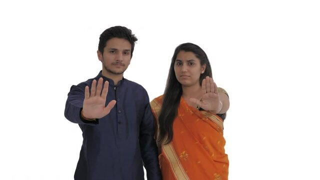 Portrait of young Indian couple flashing palms toward with straight face. Stop gesture. Isolated on white background.