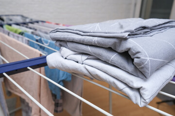 Fresh washed bed linen stacked, piled on a dryer, dry apparel on a folding portable dryer close up,...