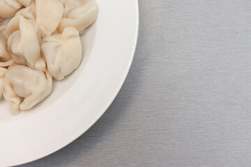 Traditional tasty boiled russian pelmeni, ravioli, dumplings with meat on white ceramic plate on grey background, copy space