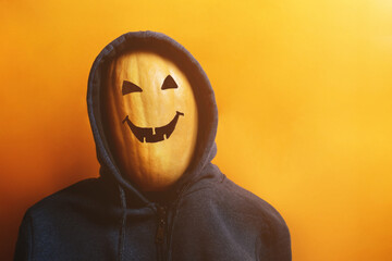 Scary pumpkin with spooky smiling face in a hoody on orange background in mist creating holiday mood. Halloween costume party and trick or treat concept.