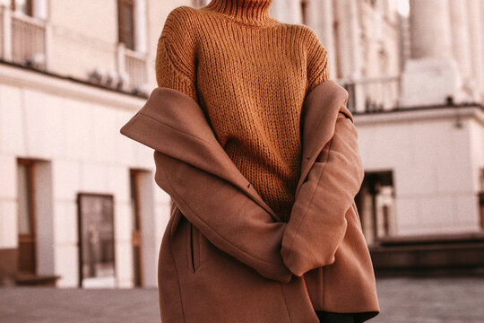 Young woman with cropped face in the orange knitted sweater and brown coat, outdoor portrait in daylight. Cozy autumn. 