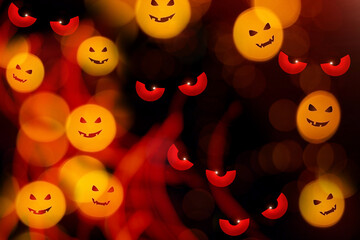 Festive blurry defocused abstract orange bokeh lights with evil pumpkin faces on black background. Halloween concept.
